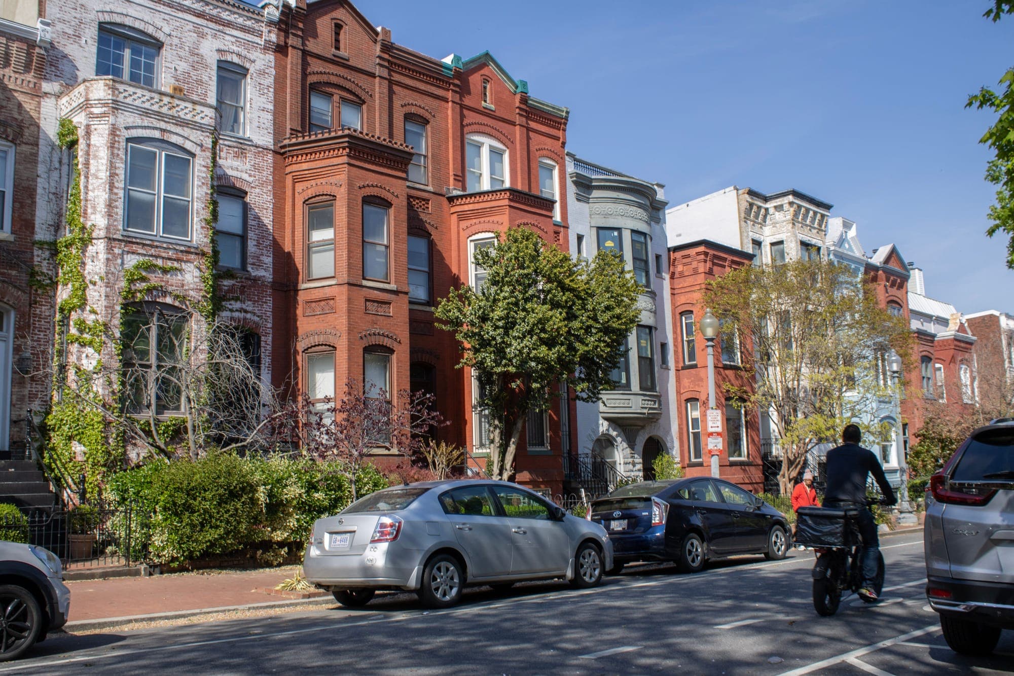 Red brick Victorian rowhouses with bay windows on a sunny Capitol Hill street in Washington, DC