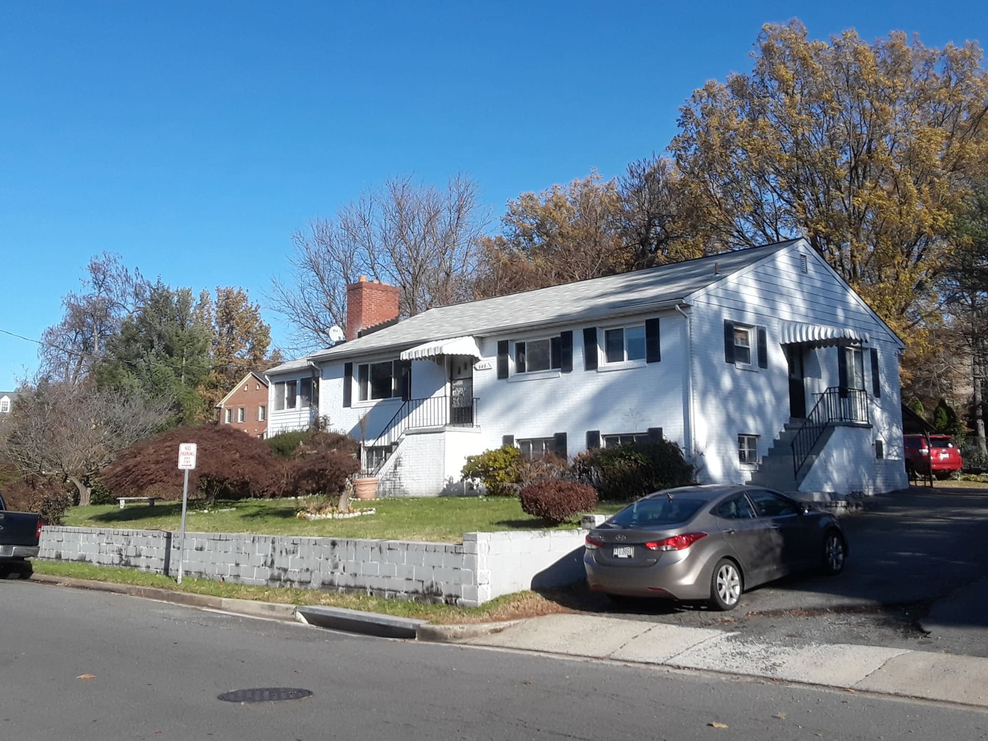 A white brick single-family home under autumn trees on a sunny street in Falls Church, Virginia